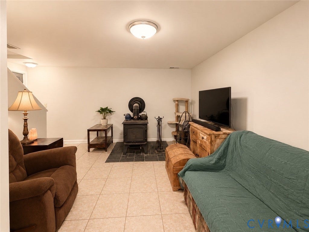 Recessed lighting, light-toned tiled flooring, wood-burning stove with a dark tile hearth, and a staircase