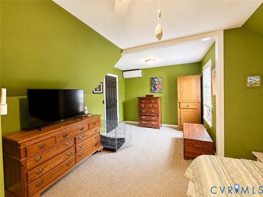 Angled ceilings, wall-mounted air conditioning unit, and textured carpet flooring