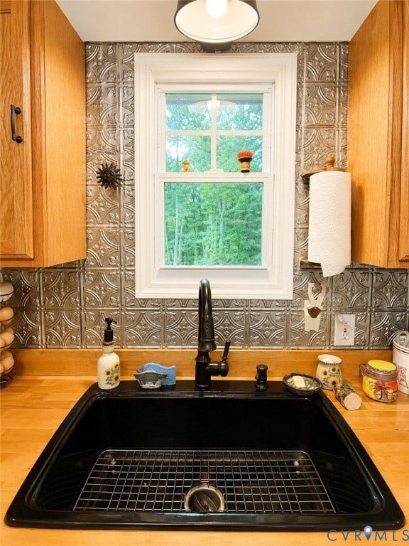 Black undermount sink with a metal grid, wood-finish countertops, black faucet, and patterned backsplash