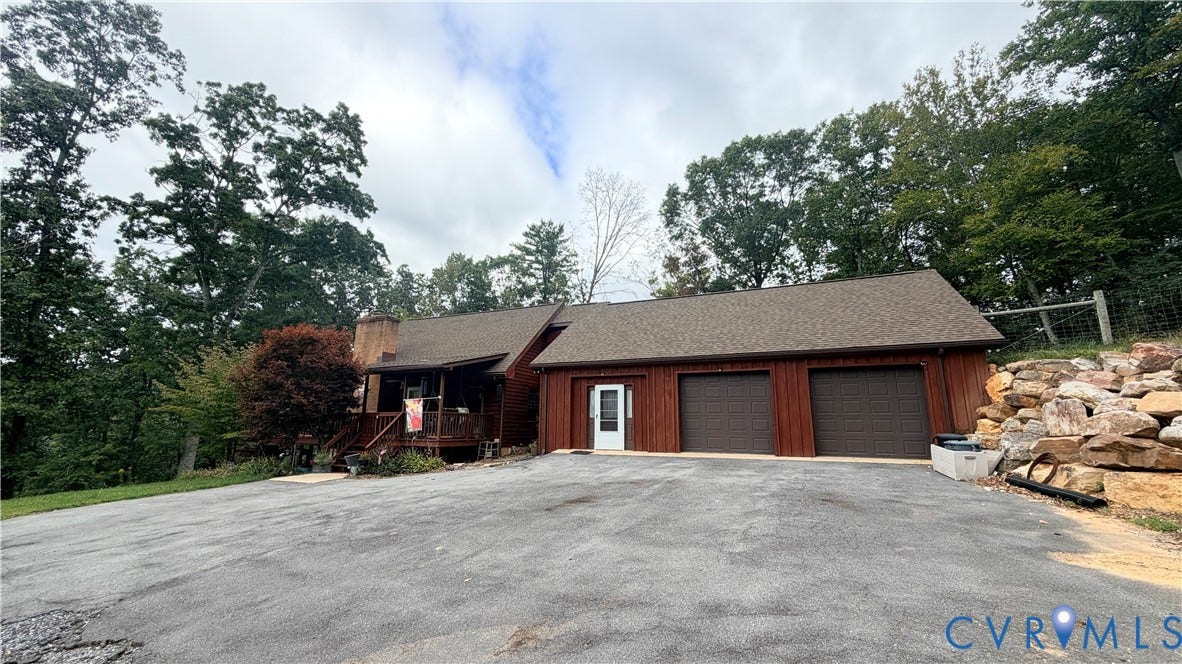 Property exterior featuring wood siding, an attached two-car garage, a covered front porch, and a stone retaining wall