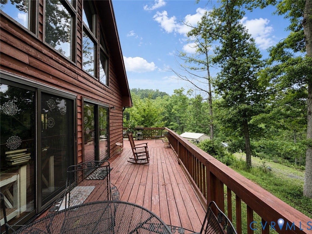 Expansive wood deck with a matching wood railing, multiple sliding glass doors, and upper-level windows