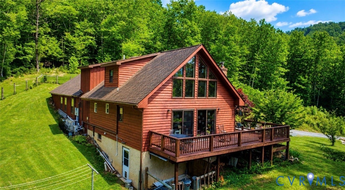 Wood-sided exterior featuring an expansive outdoor deck, floor-to-ceiling windows, and a surrounding wooded landscape