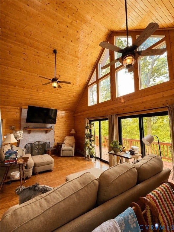 Vaulted ceiling with wood paneling, wood-finish flooring, full-height windows, fireplace with white surround, and sliding glass doors to outdoor decking