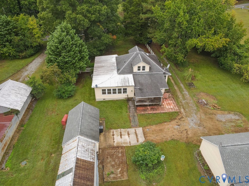 Aerial perspective showcasing the primary residence, two detached outbuildings, a gravel driveway, and surrounding mature trees