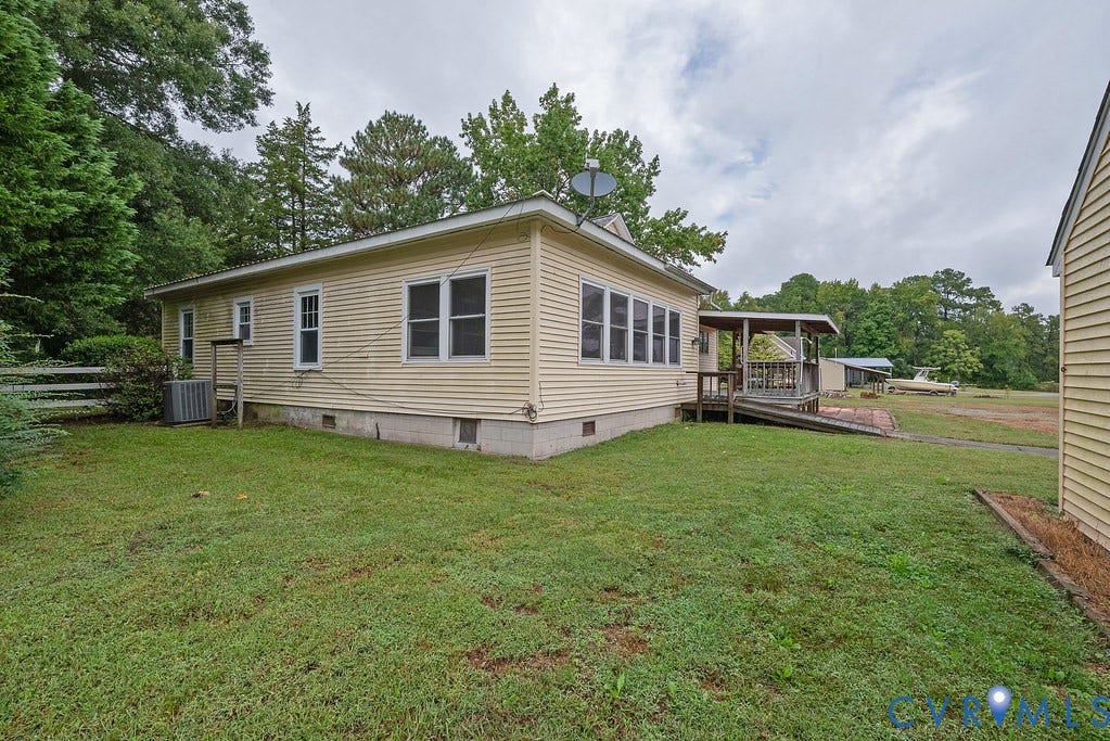 Single-story residence featuring light-colored siding, multiple windows, a covered wood deck, and a wood ramp