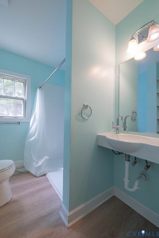 Wall-mounted sink with chrome fixtures, wood-finish flooring, and a shower with a privacy curtain