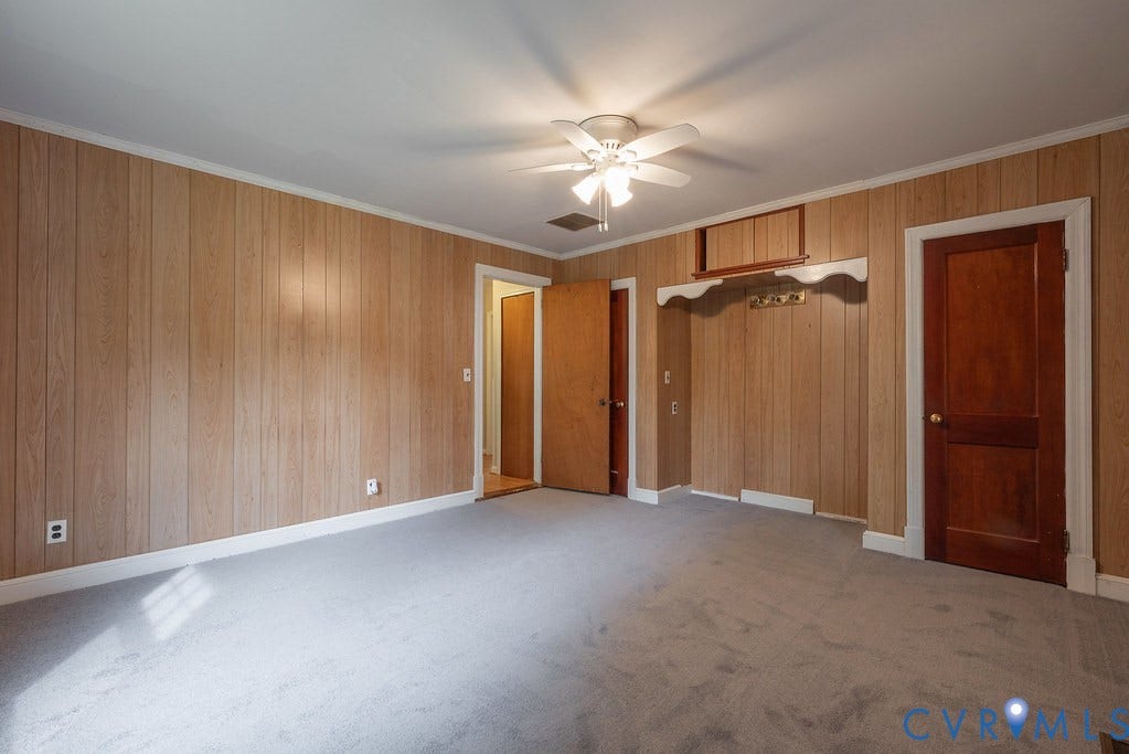 Carpeted flooring, paneled wall finish, white trim, wood-finish doors, and a ceiling fan with integrated lighting