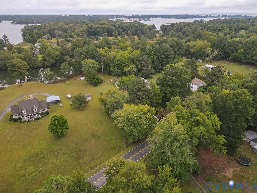 Expansive lot featuring a large home with a circular driveway, multiple outbuildings, mature trees, and waterfront access