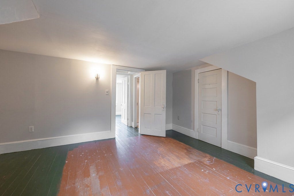 Exposed wood flooring, painted white trim, white paneled doors, and wall-mounted lighting