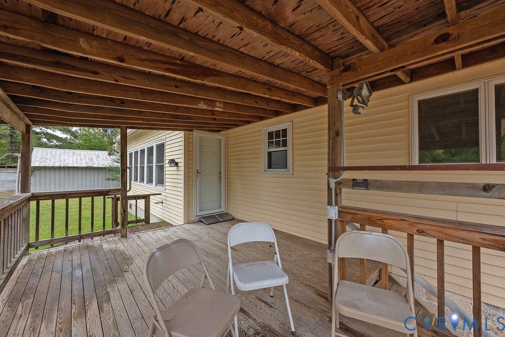 Expansive covered wooden deck featuring exposed wood ceiling beams and a wooden railing