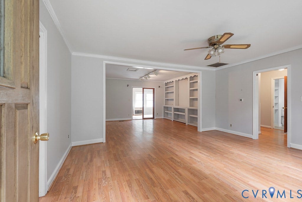 Wood-finish flooring throughout, featuring a ceiling fan with integrated lighting, built-in shelving, and white crown molding