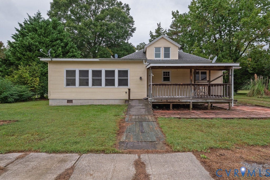 Cream-colored siding exterior with a covered porch, wood deck, and a red brick patio