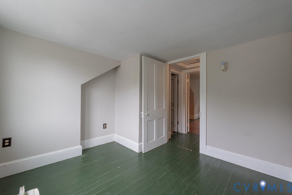 White painted walls with sloped ceiling detail, painted wood flooring, and white trim molding