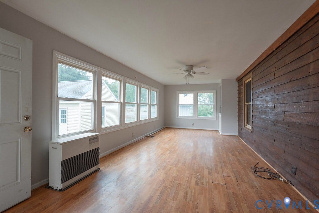 Expansive room featuring wood-finish flooring, a wall of multiple windows, a ceiling fan, and a rustic wood panel accent wall