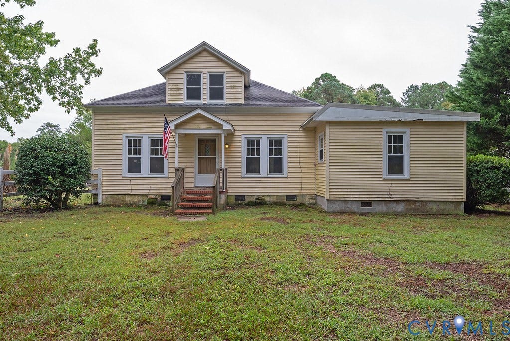 Yellow siding exterior with multiple windows, a front porch with wood railings, and a dormer window
