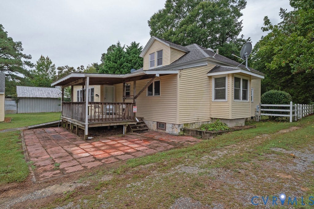 Exterior featuring light-toned siding, a covered porch, an adjacent patio area, a bay window, and a white picket fence