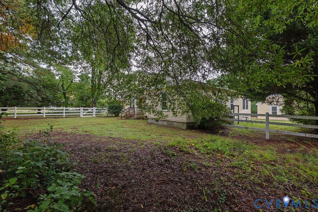 Expansive outdoor space featuring a white split-rail fence, mature trees, and a visible portion of the property's exterior
