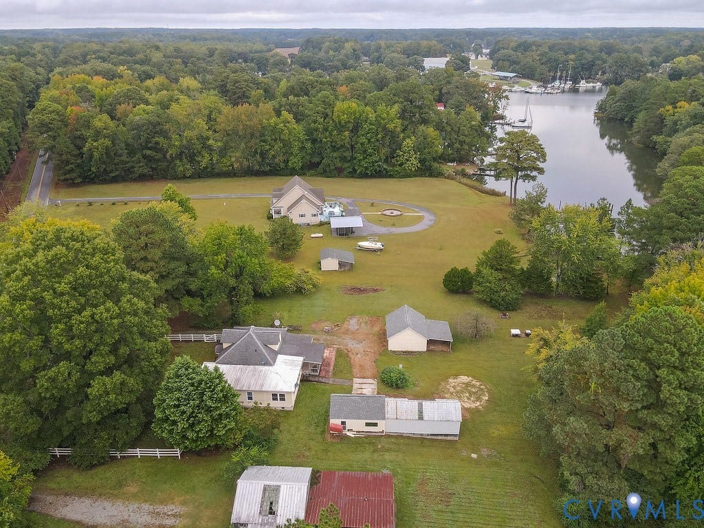 Waterfront property featuring multiple structures, mature trees, and expansive green space