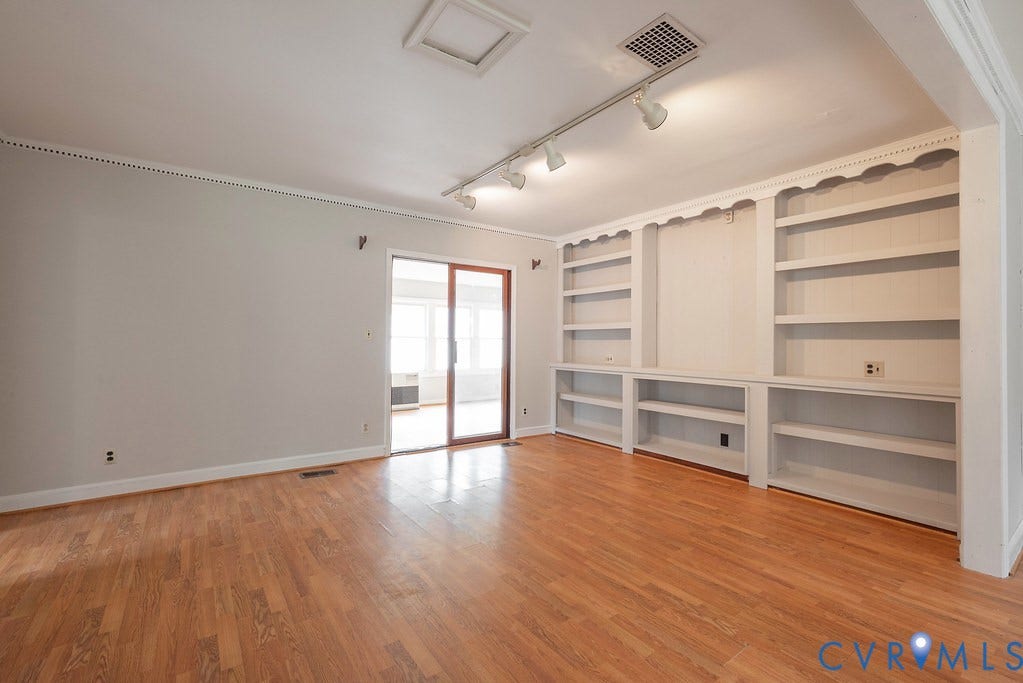 Wood-finish flooring, built-in shelving, crown molding, track lighting, and sliding glass doors