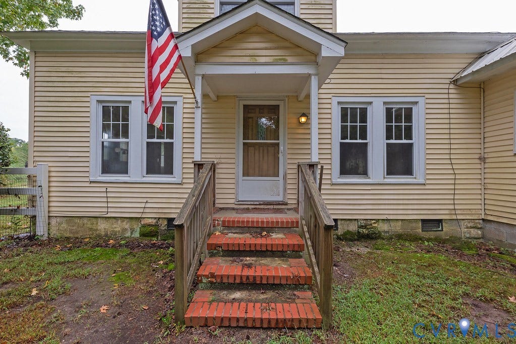 Wood siding exterior with brick foundation, covered porch entry, brick steps with wood railings, and multi-pane windows