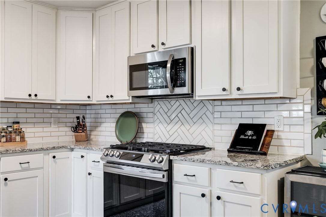 White shaker cabinetry, stainless steel microwave, stainless steel range, light-colored granite countertops, and white subway tile backsplash with a herringbone accent