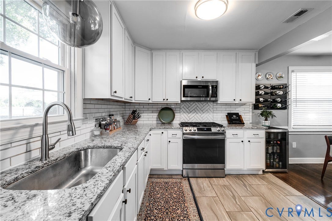 White cabinetry, stone countertops, stainless steel appliances, tile backsplash, and wood-finish flooring