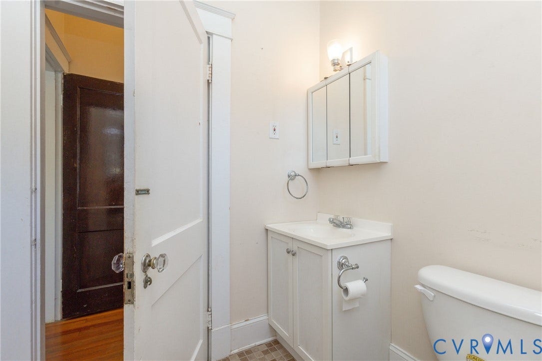 Bathroom featuring a white vanity cabinet with an integrated sink, tri-fold medicine cabinet, wall-mounted light fixture, and classic glass door hardware