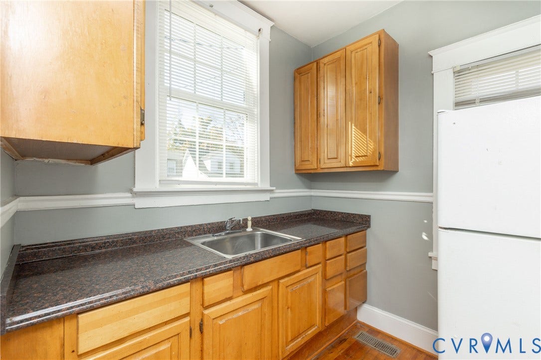 Kitchen featuring natural wood cabinetry, dark stone-finish countertops, stainless steel sink with metal faucet, and windowed walls