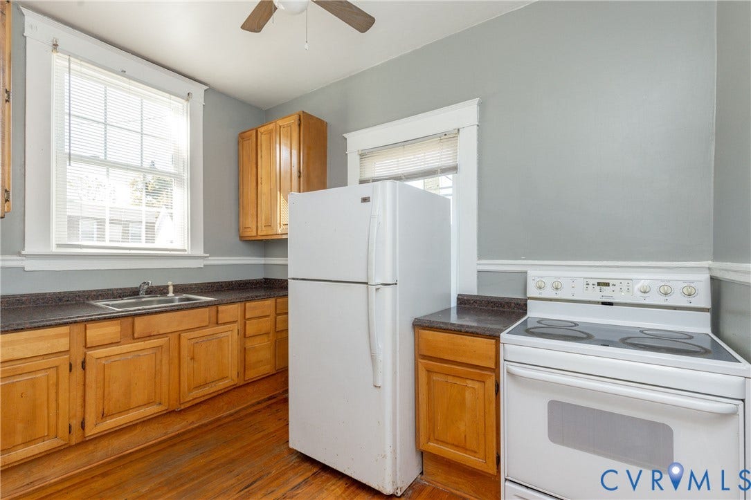 Kitchen featuring natural wood cabinetry, dark laminate countertops, white appliances, and hardwood flooring