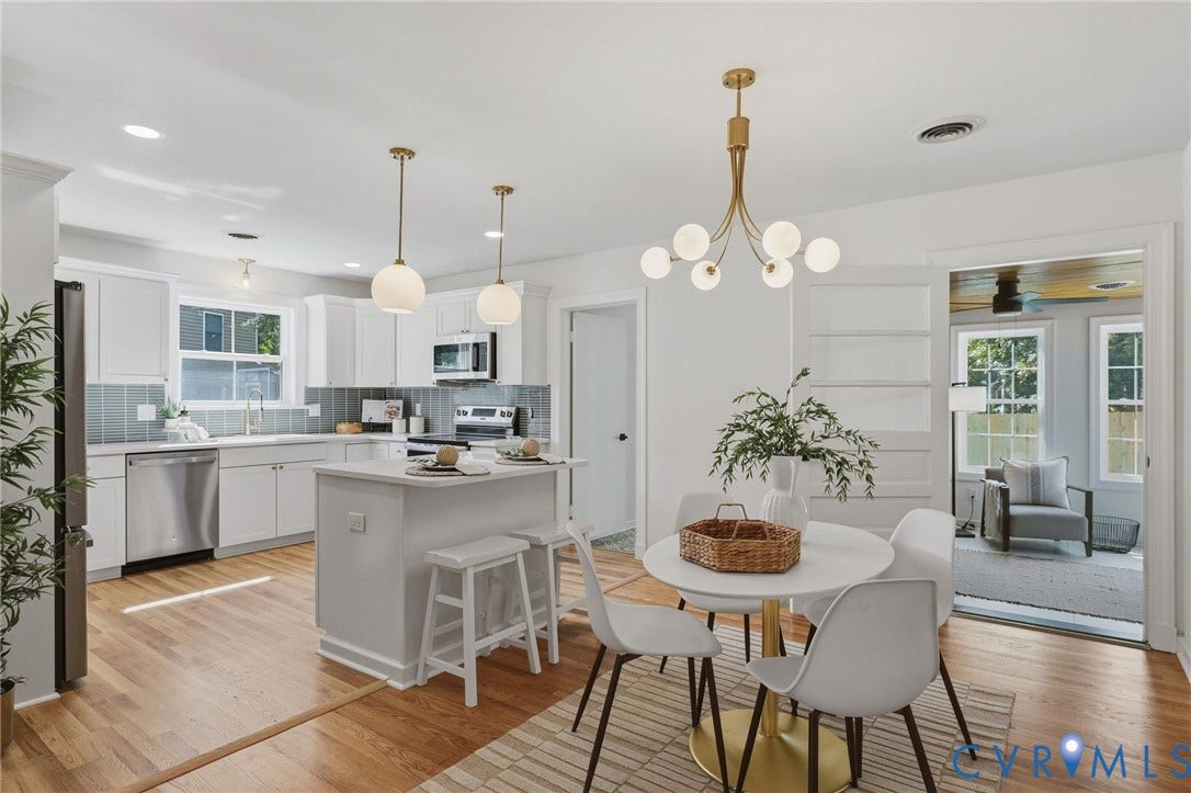 Bright kitchen with wood-finish flooring, white cabinetry, stainless steel appliances, and a central island with seating