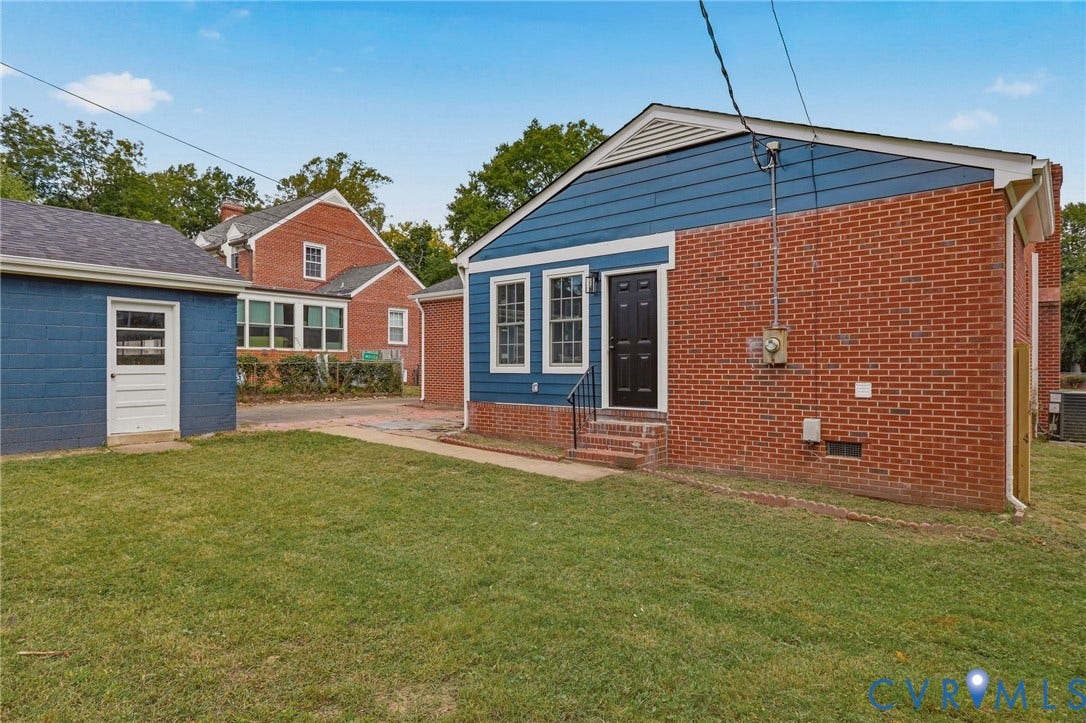 Brick and siding exterior with a dark-paneled entry door, adjacent to a detached structure with a white entry door