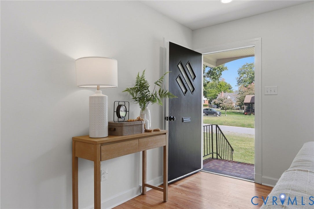 Hardwood-finish flooring, white walls, black front door with decorative paneling, black metal railing, and a clear glass storm door