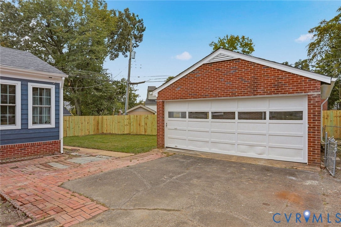 Detached brick garage with a paneled door, wood privacy fencing, and a paved driveway