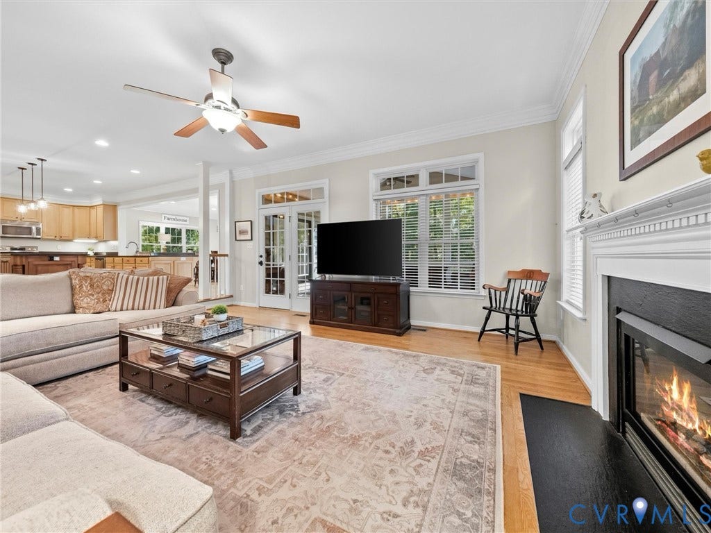 Living space featuring wood-finish flooring, a fireplace with a white mantel, and a ceiling fan