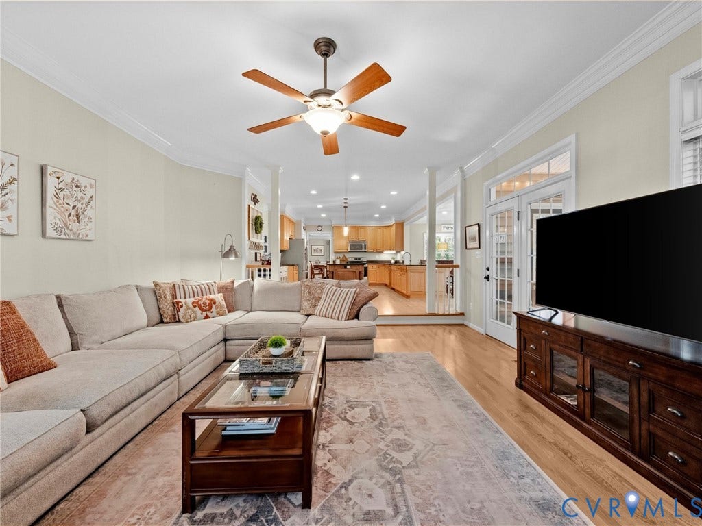 Wood-finish flooring throughout, ceiling fan with integrated lighting, crown molding, and double glass-paneled doors with transom windows