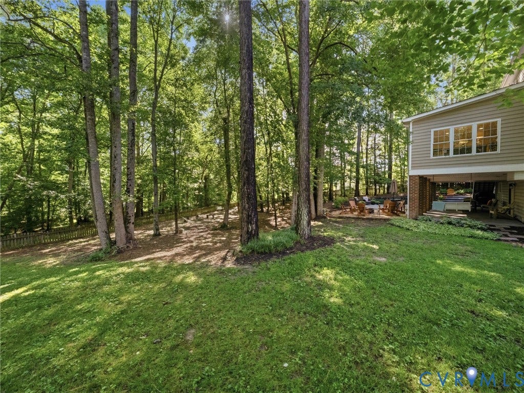 Expansive rear yard with mature trees, a wooden fence, and a lower-level covered patio