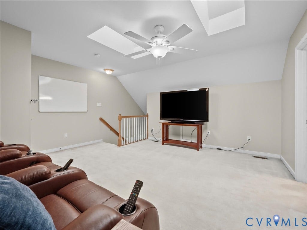 Carpeted room with a ceiling fan, sloped ceiling, and wood banister