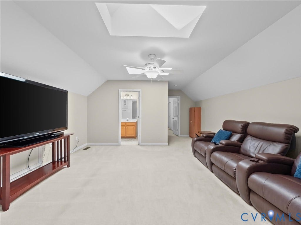 Vaulted ceiling with skylight and ceiling fan, neutral carpet flooring, and access to a bathroom with a wood-finish vanity
