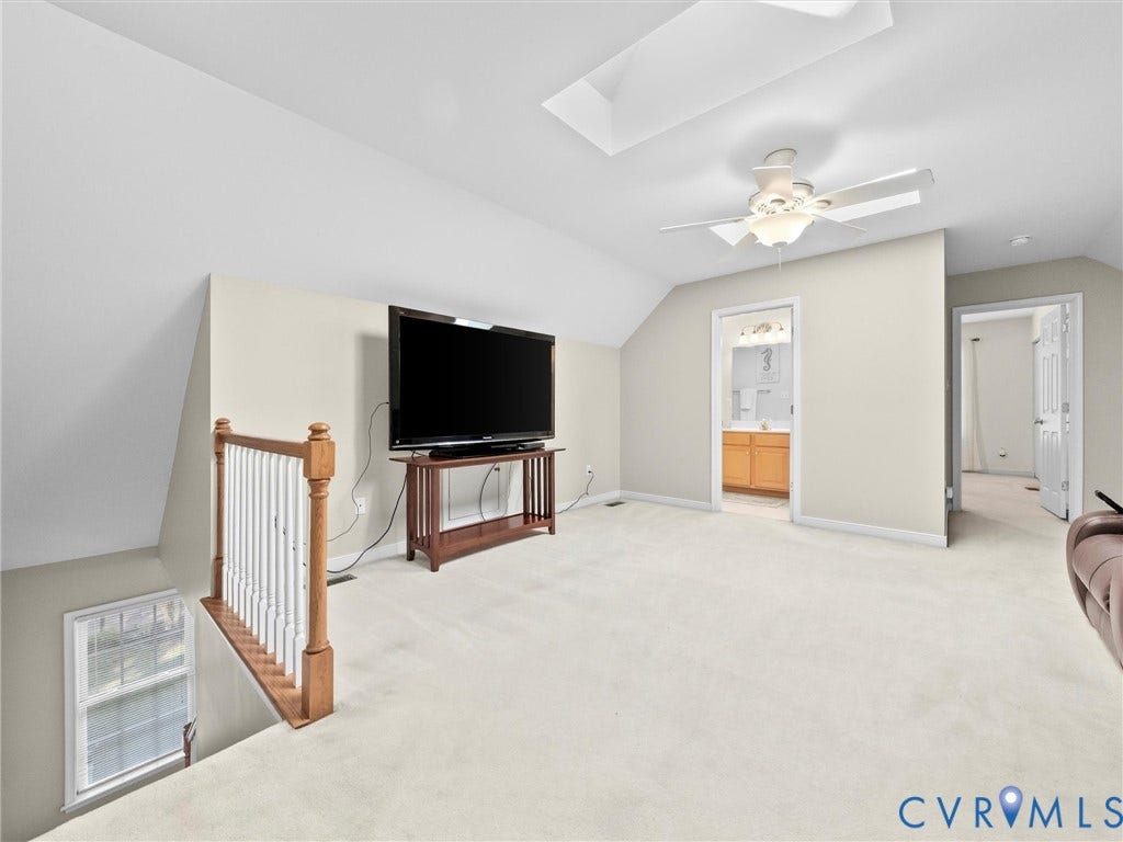 Carpeted loft space with a vaulted ceiling, ceiling fan, and wood railing