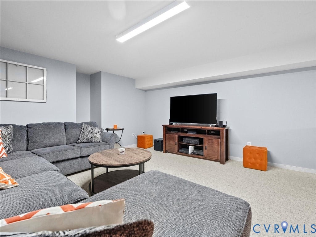 Spacious finished basement featuring a generous open layout with neutral carpeting, recessed and linear ceiling lighting, and a built-in media console with wood-finish cabinetry and shelving