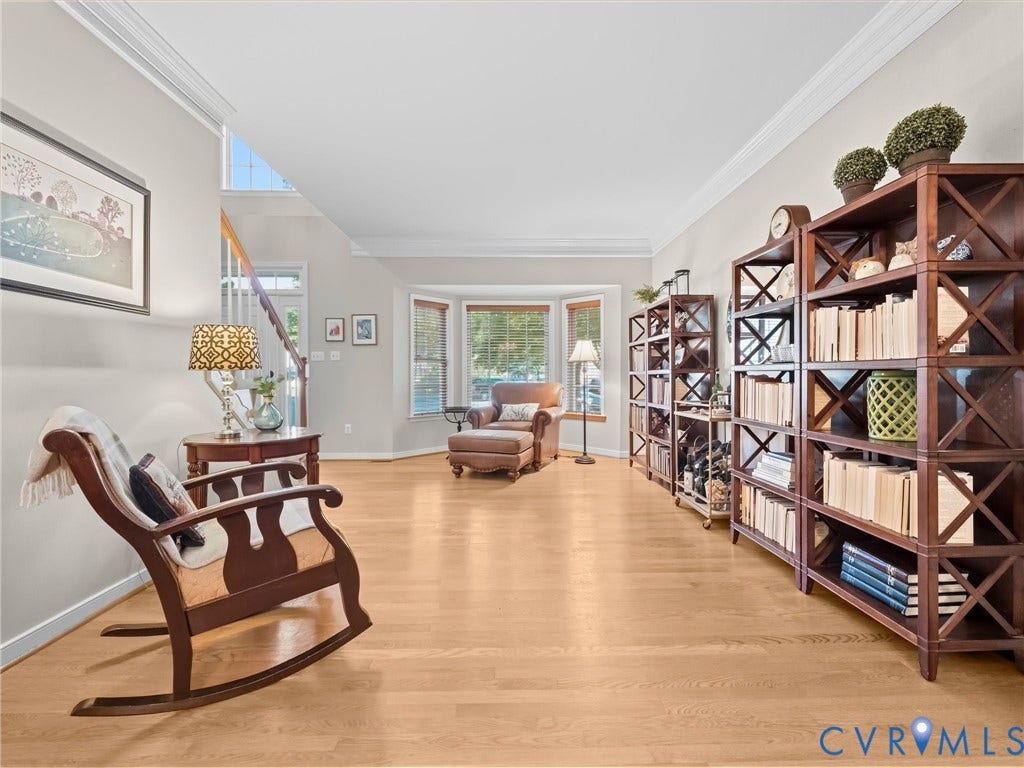 Hardwood flooring, bay window, built-in shelving, crown molding, and a visible staircase