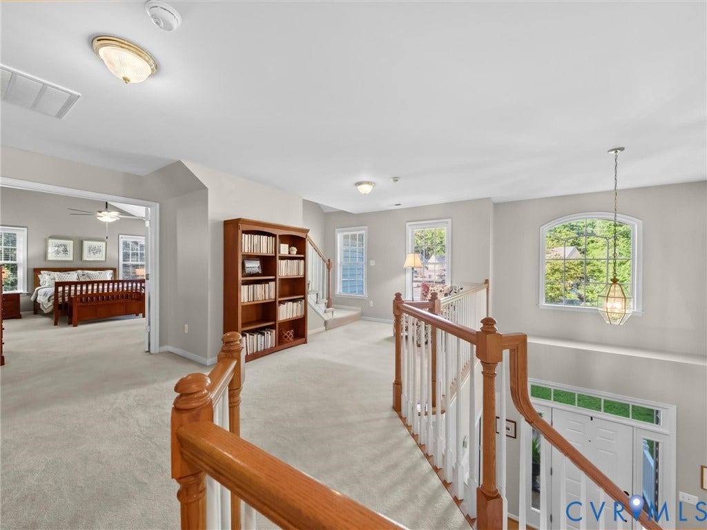 Carpeted landing with built-in wooden shelving, multiple windows, and a staircase featuring wood railings and white balusters