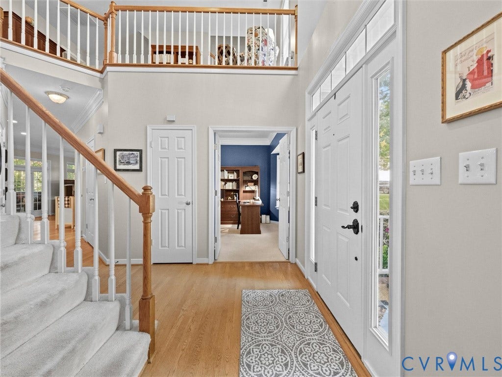 Two-story foyer with hardwood flooring, carpeted staircase, and an upper-level balcony with wood railings