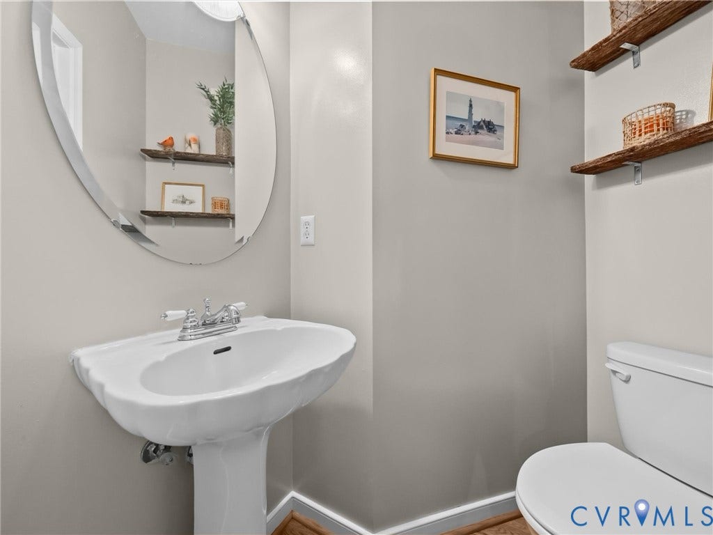 Pedestal sink with chrome faucet, oval frameless mirror, and wall-mounted shelving