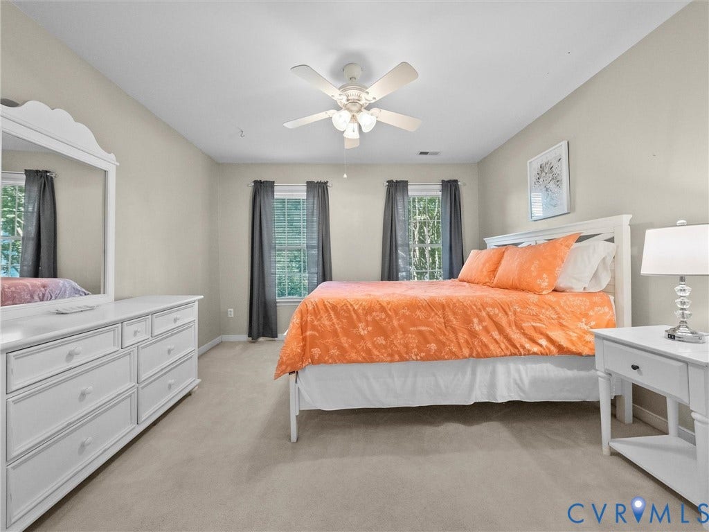 Spacious primary bedroom with neutral wall finishes, carpeted flooring, and abundant natural light from multiple windows dressed with gray drapery