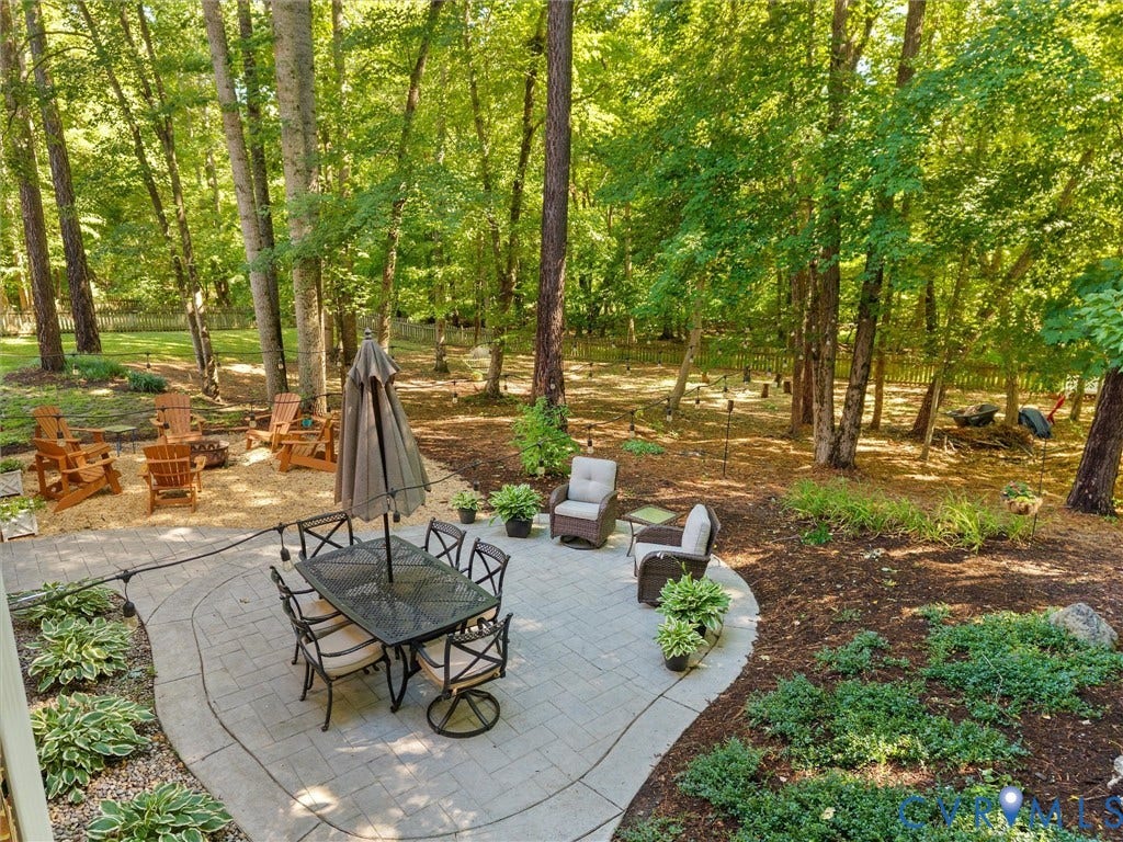 Expansive backyard featuring a paver patio with a dining area, a separate fire pit area, and mature trees