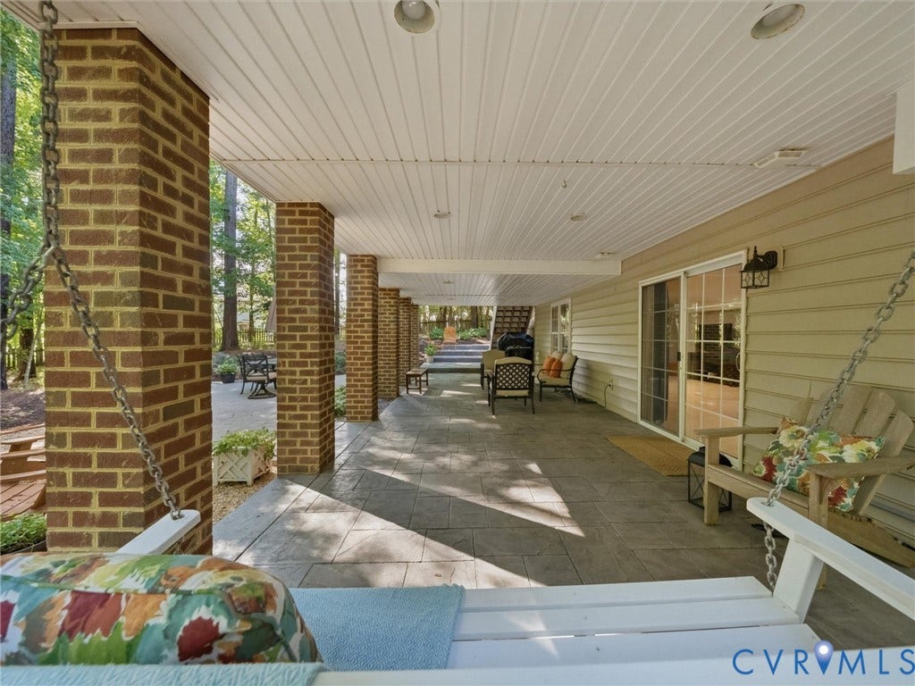 Expansive covered patio with brick support columns, recessed lighting, and a sliding glass door entry