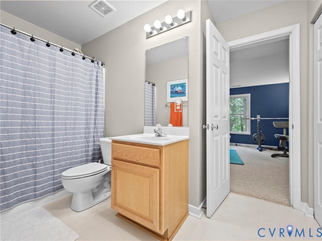 Bathroom featuring a single vanity with wood-finish cabinetry, a toilet, and a shower-tub combination