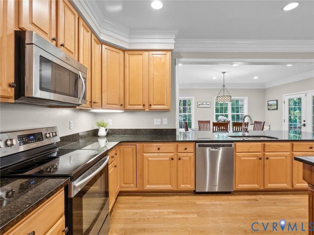 Wood-finish flooring, stainless steel appliances, dark stone countertops, wood cabinetry, and recessed lighting