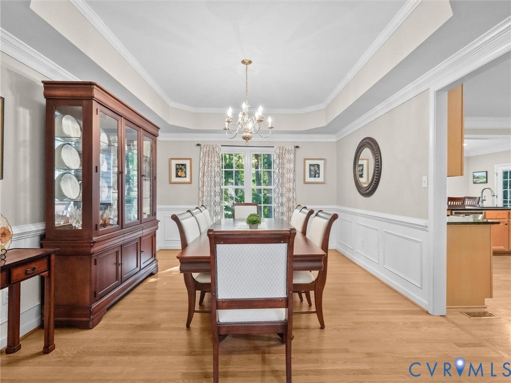 Elegant formal dining room showcasing hardwood flooring, a coffered ceiling with crown molding, and a crystal chandelier